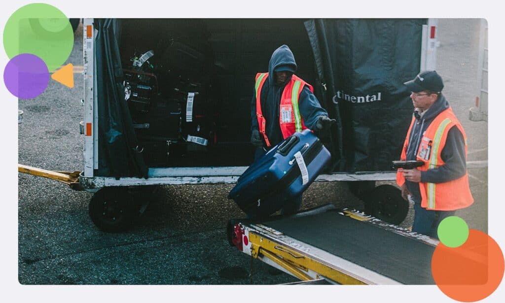 An airfield baggage handler moving a suitcase 