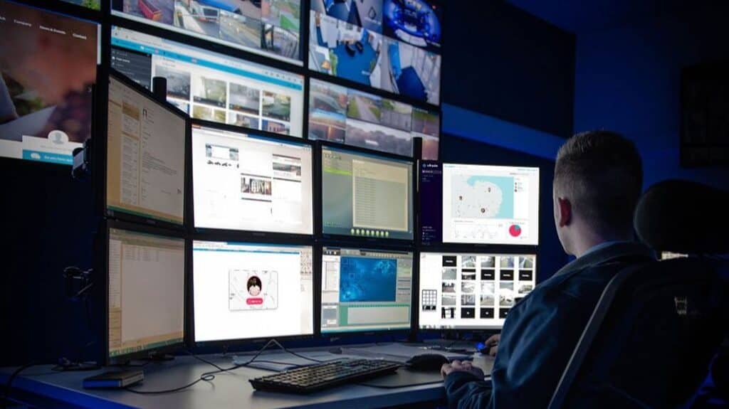 An alarm receiving centre employee in front of a number of screens used for emergency response