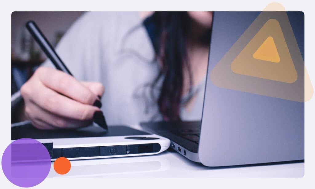 A staff member making notes on a tablet whilst sat at a laptop