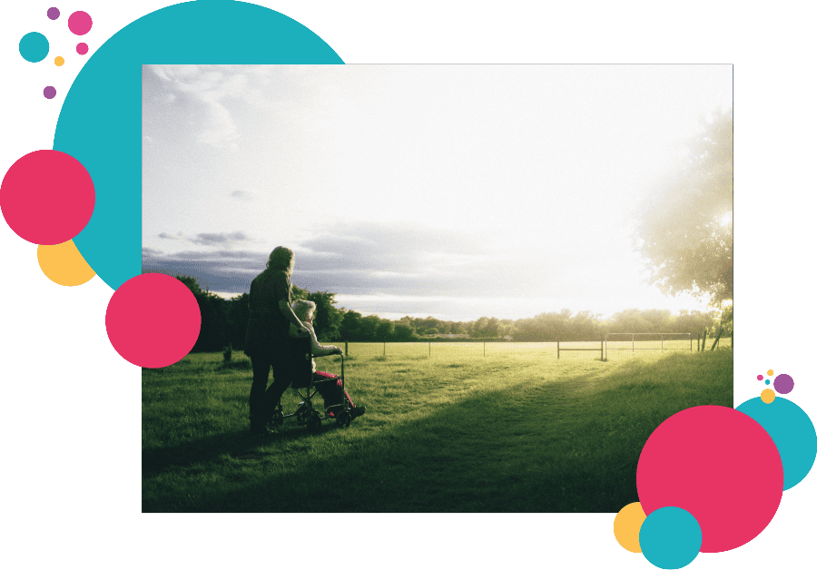 A healthcare lone worker pushing an elderly person in a wheelchair through a park