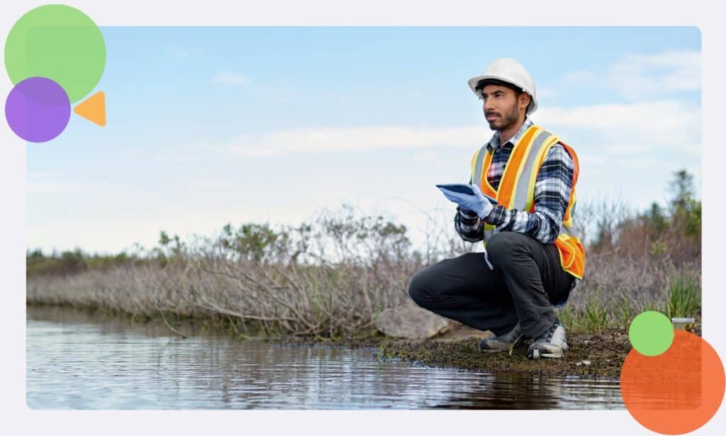 A staff member with no colleagues nearby crouching alone on a river bank