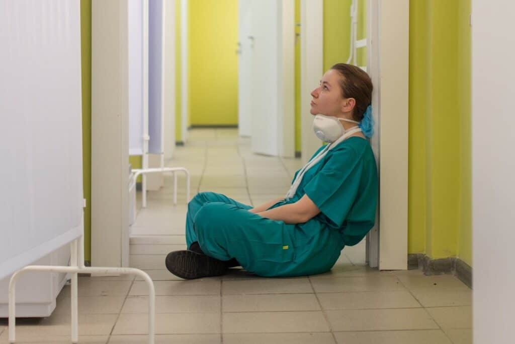 A stressed looking healthcare worker sitting on the floor of a hospital