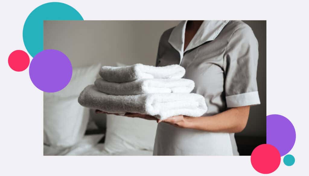 A lone working hotel maid or cleaner carrying towels in a hotel room