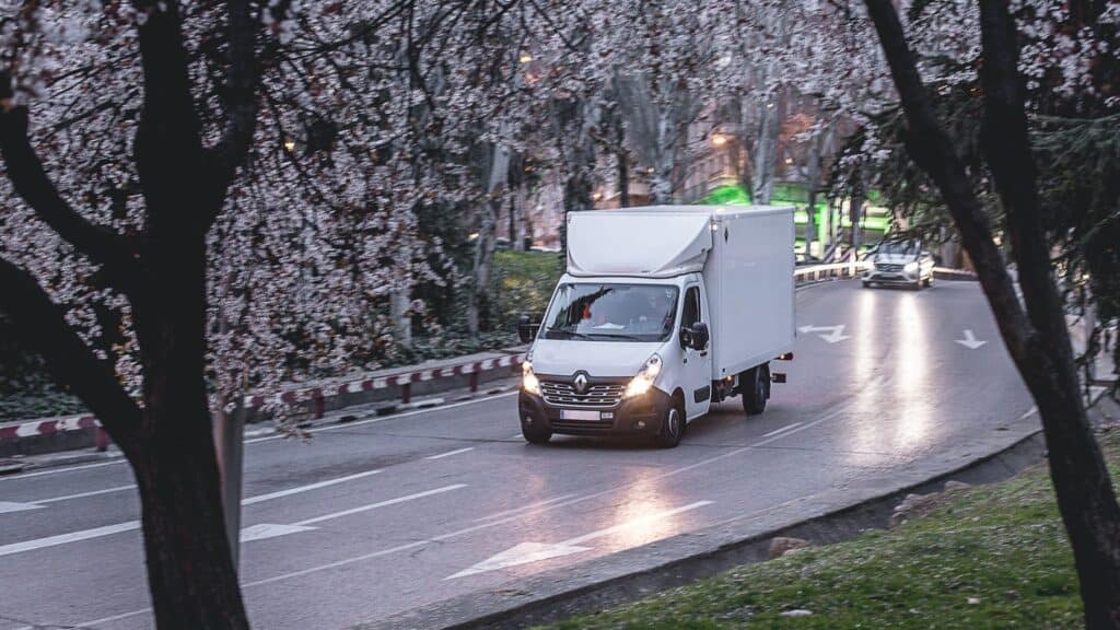 A white van on a road as seen through blossoming trees