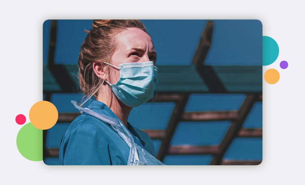 A medical staff member standing alone outside with a facemask and apron on