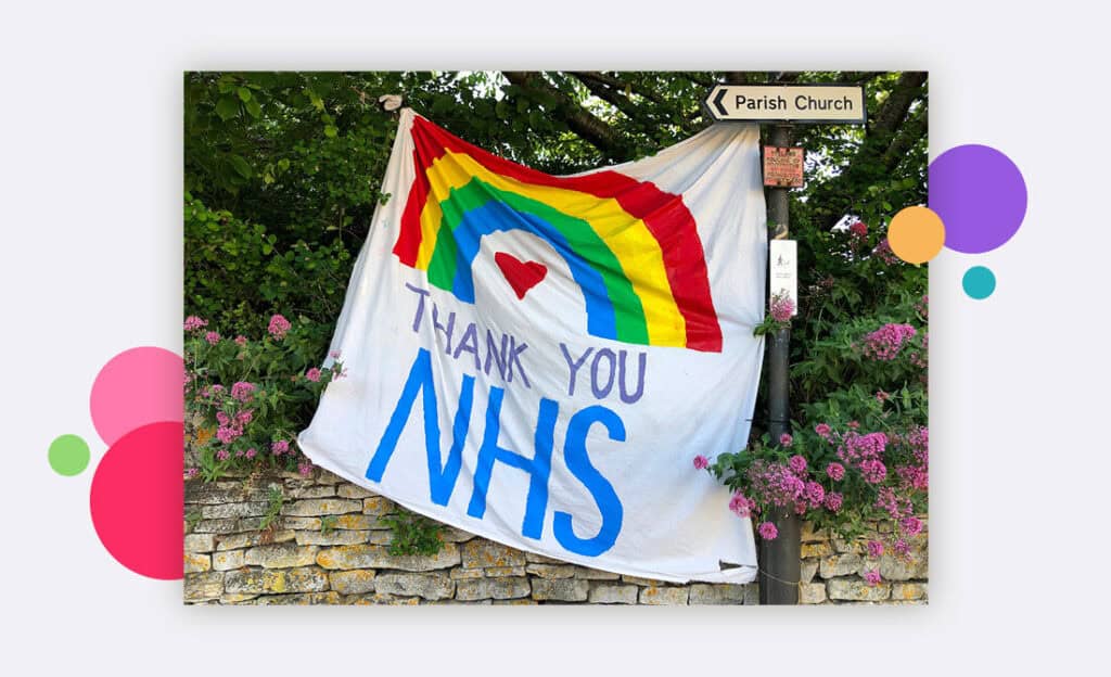 A hand painted flag tied to a tree that says thank you NHS with a rainbow