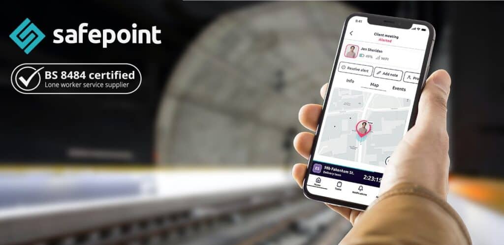 A hand holding up the safepoint lone working mobile app in a railway worker scene with an icon highlighting the system is BS8484 accredited